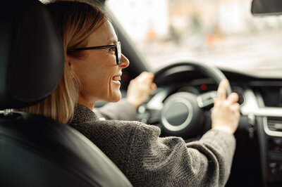 Eine Frau sitzt freudig am Steuer ihres Fahrzeugs, dass sie mit einem Auto Abo Vergleich gefunden hat.